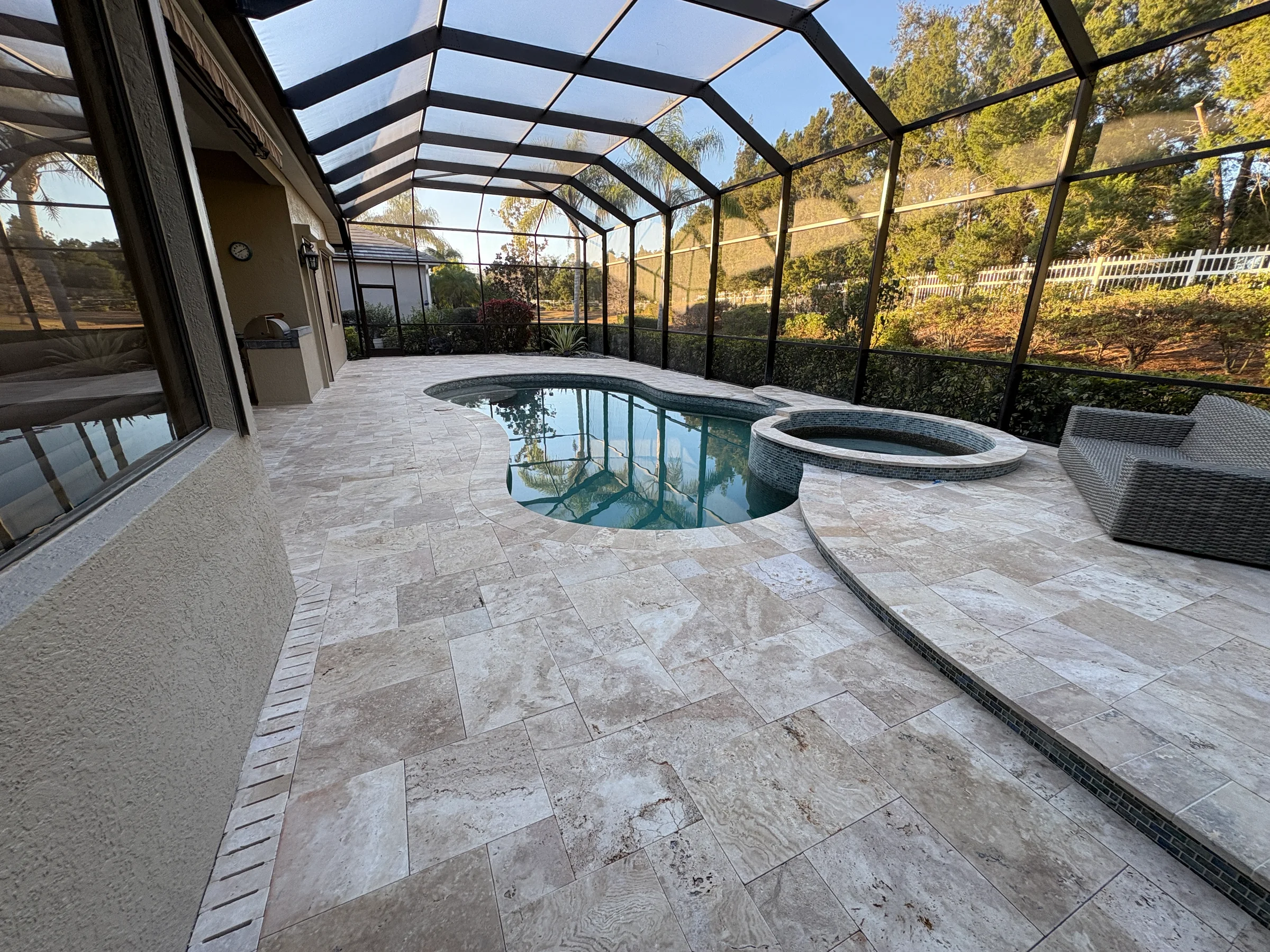 Light natural-stone pool deck inside a screen enclosure